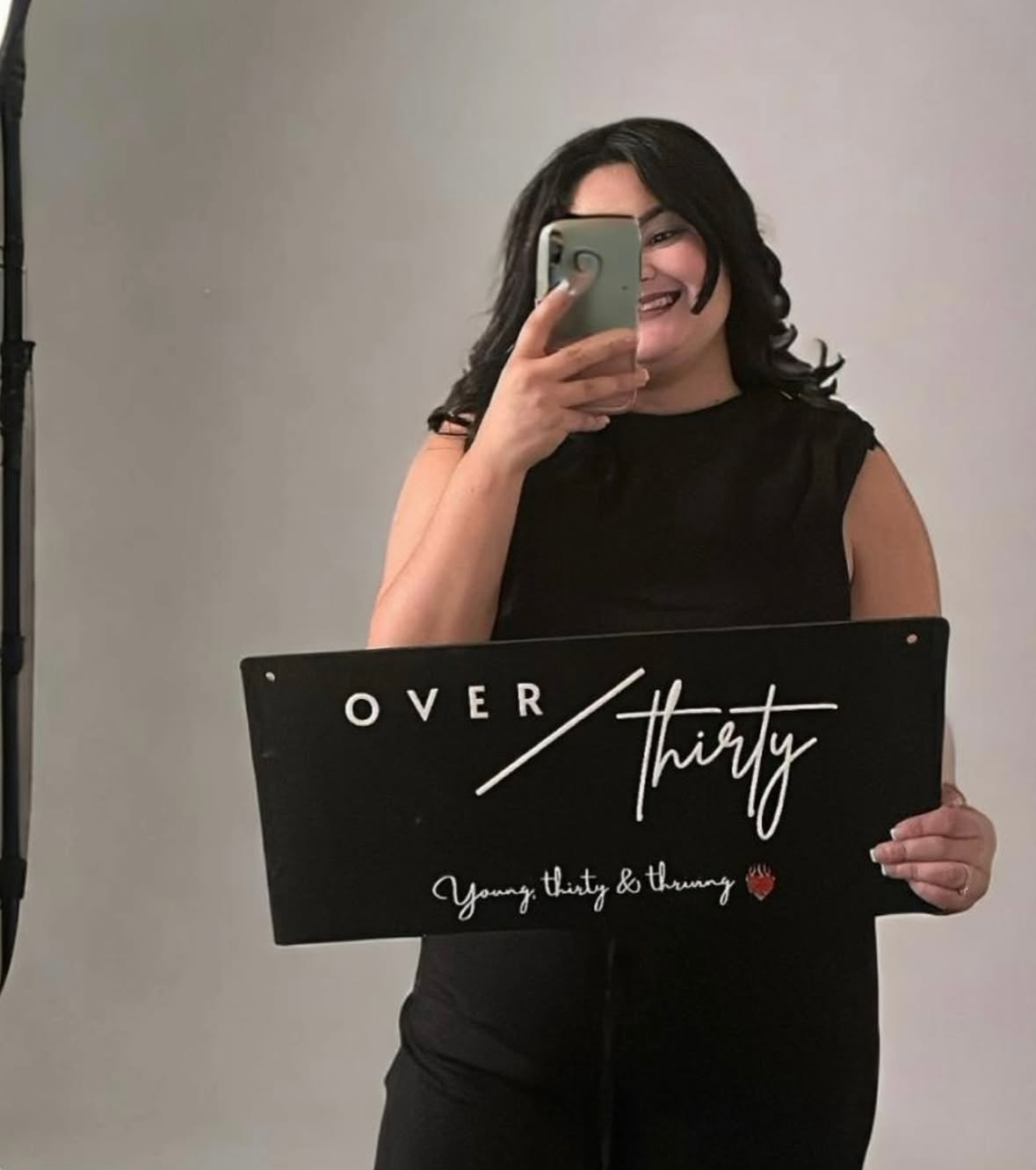 Person holding a sign with 'Over Thirty' text, standing in front of a gray background